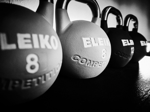 Schwarz-Weiß-Foto von vier in einer Reihe aufgereihten ELEIKO-Wettkampf-Kettlebells, mit sichtbaren Gewichtsmarkierungen von 8 und 12 Kilogramm. Der Fokus liegt auf der vorderen Kettlebell.