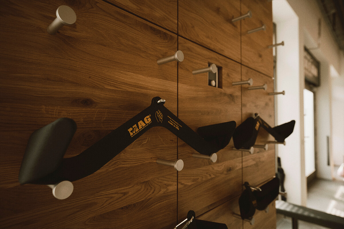 Nahaufnahme von schwarzen und gelben Klettergriffen, die an einer hölzernen Turnhallenwand montiert sind und aus denen Metallpflöcke herausragen, um die Griffkraft zu trainieren. Der Hintergrund zeigt einen Korridor mit natürlichem Licht.